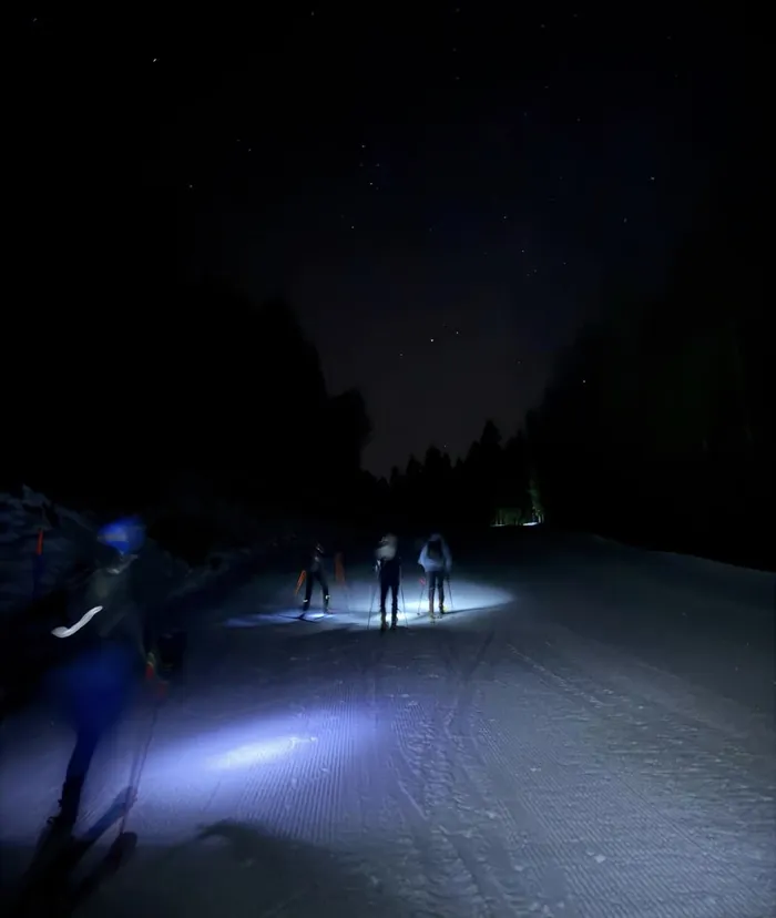 Scialpinisti con la frontale sulla pista di notte